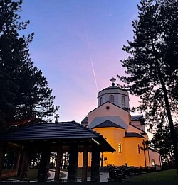 ноћни снимак храма преображења господњег обасјаног декоративном расветом док пахуље снега падају на камену фасаду и звоник